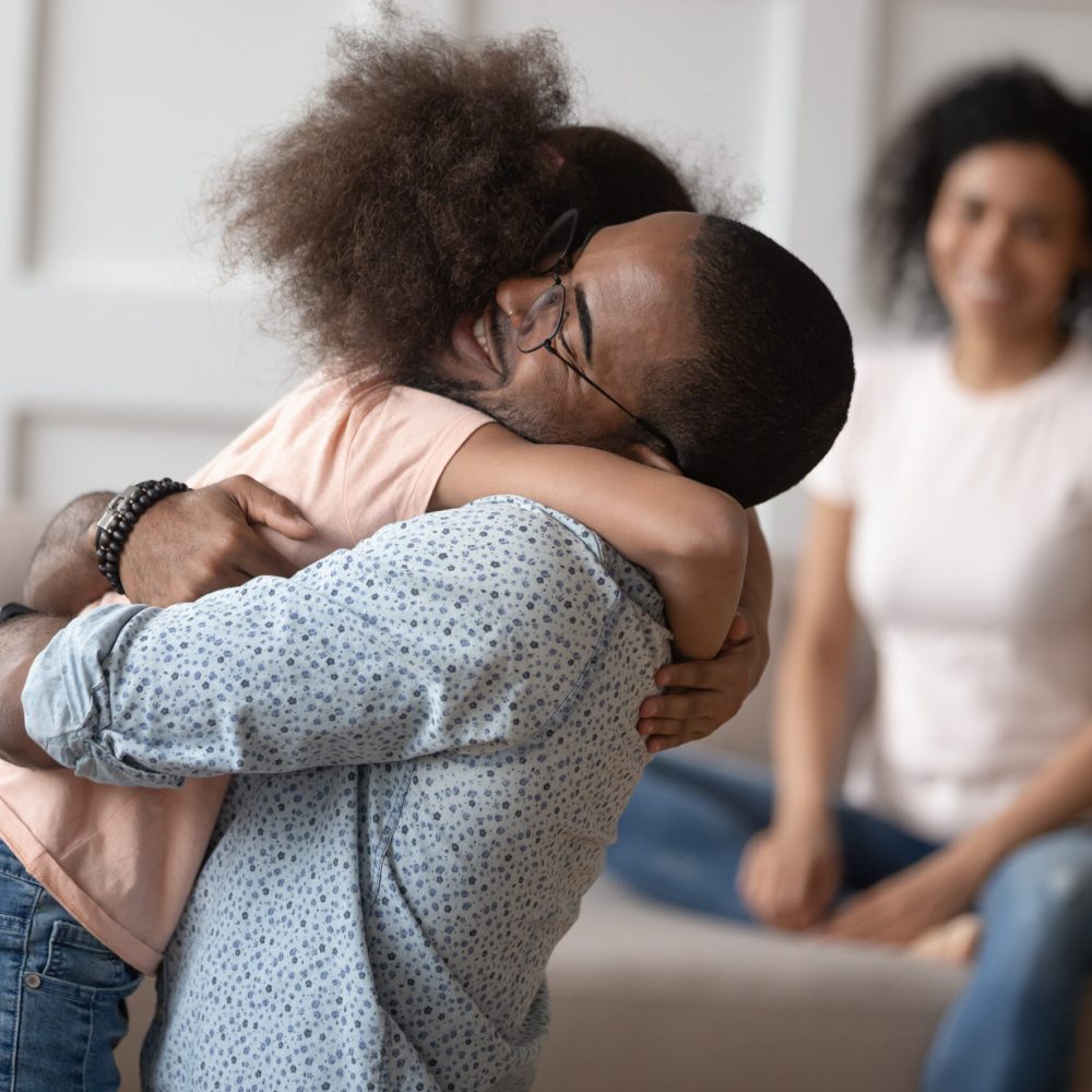 Happy little girl hug dad reunited after separation Happy little biracial girl hug loving african American dad meeting him at home after work business trip, overjoyed mixed race kid embrace black father reunited with smiling mom. Family reunion concept